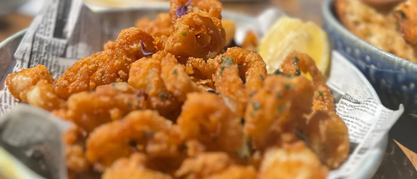 Plat de calamars frits croustillants sur du papier journal, avec un quartier de citron