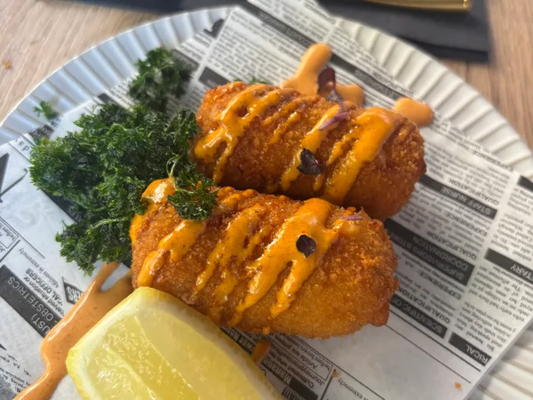 Deux croquettes sur du papier journal avec un quartier de citron et une sauce relevée