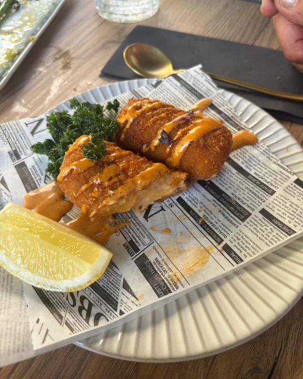 Twee kroketten op krantenpapier met een partje citroen en pittige saus