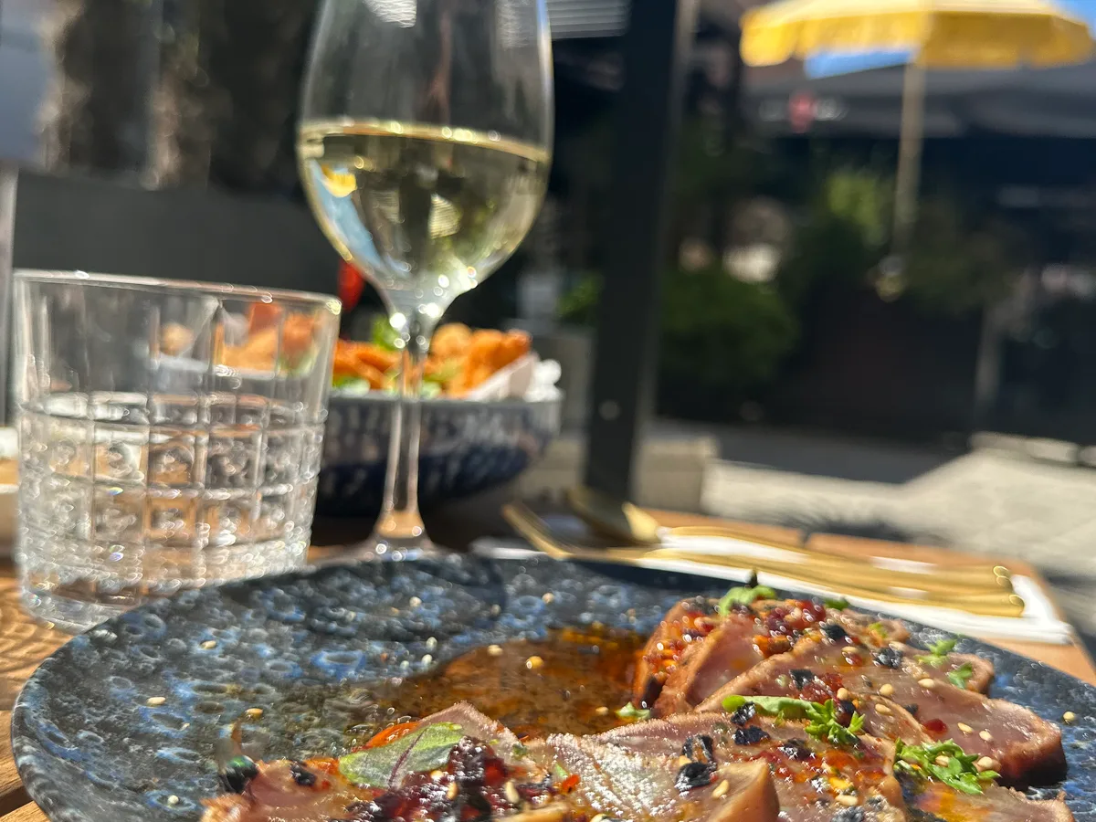 Assiette de poisson finement tranché et verre de vin blanc en terrasse