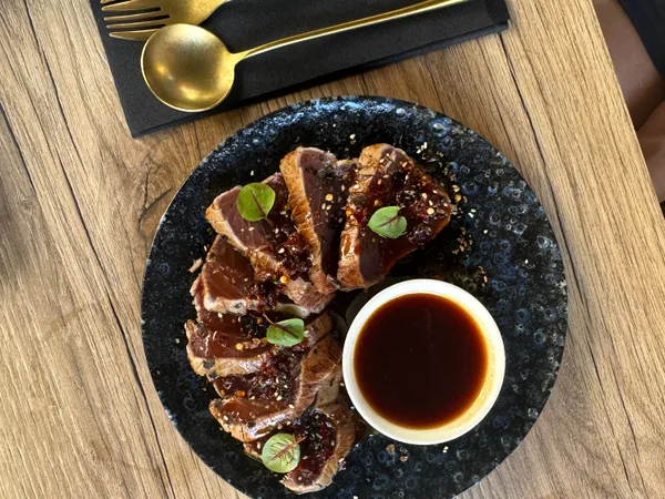 Viande finement tranchée au sésame autour d’un bol de sauce brune